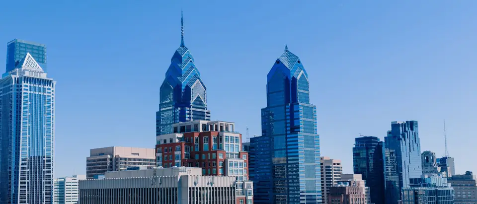 Glass office towers in Center City Philadelphia, among them the two peaked Liberty Place towers, against a clear blue sky